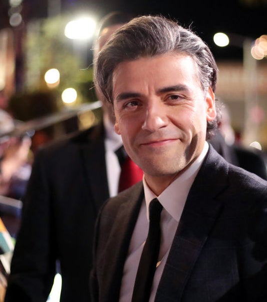 Oscar Isaac, clean shaven, wearing a suit on the red carpet and smiling for camera