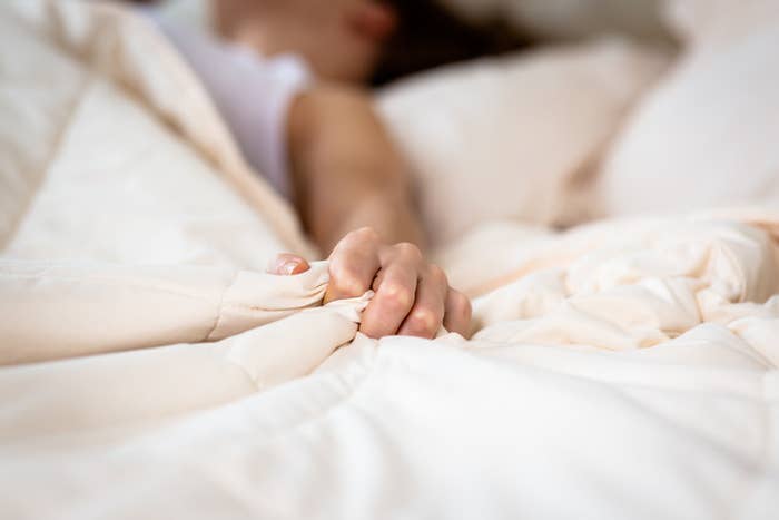 Close up of a woman&#x27;s hand grasping her bedsheets