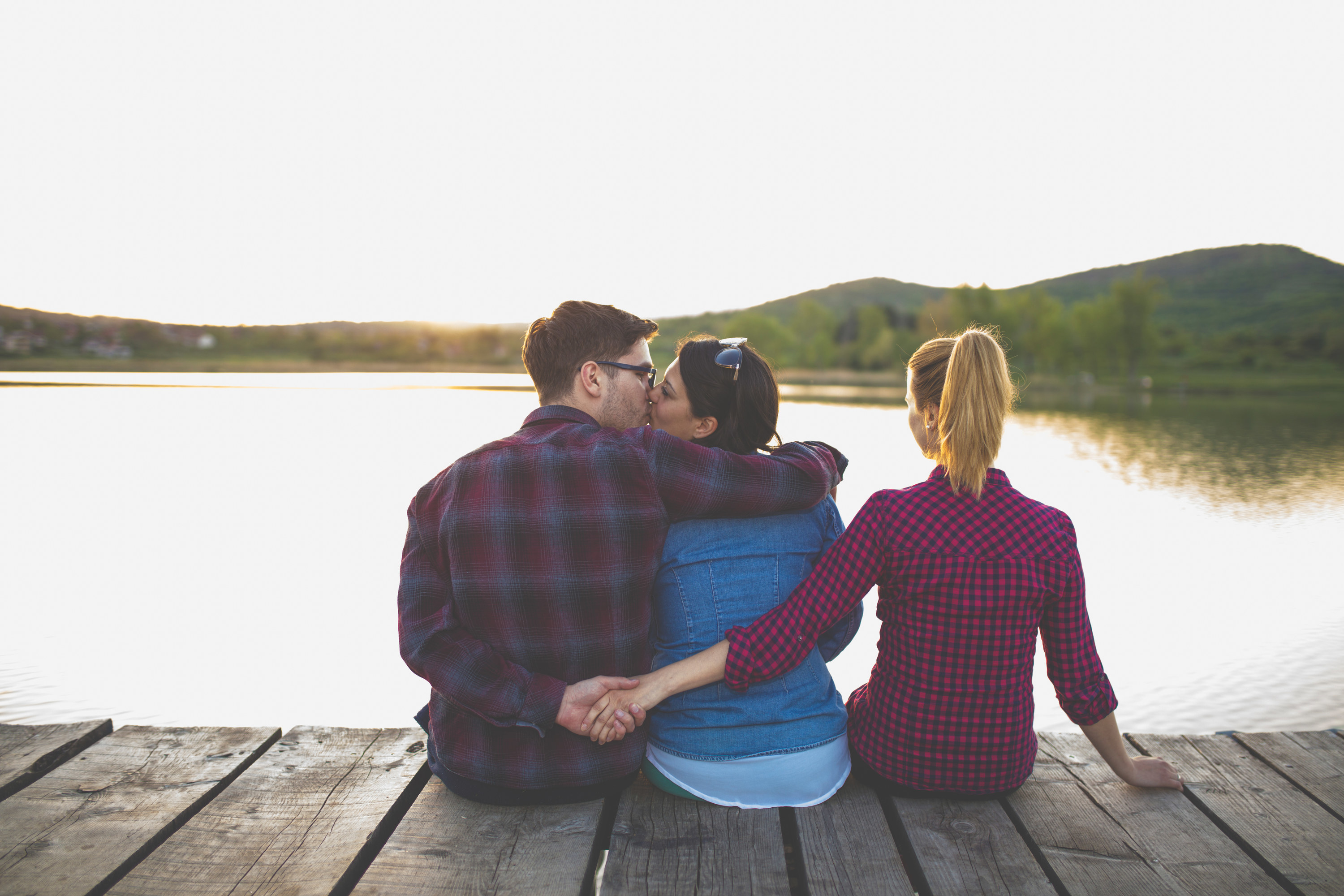 An image of a couple embracing while the man holds the hand of someone else behind their back