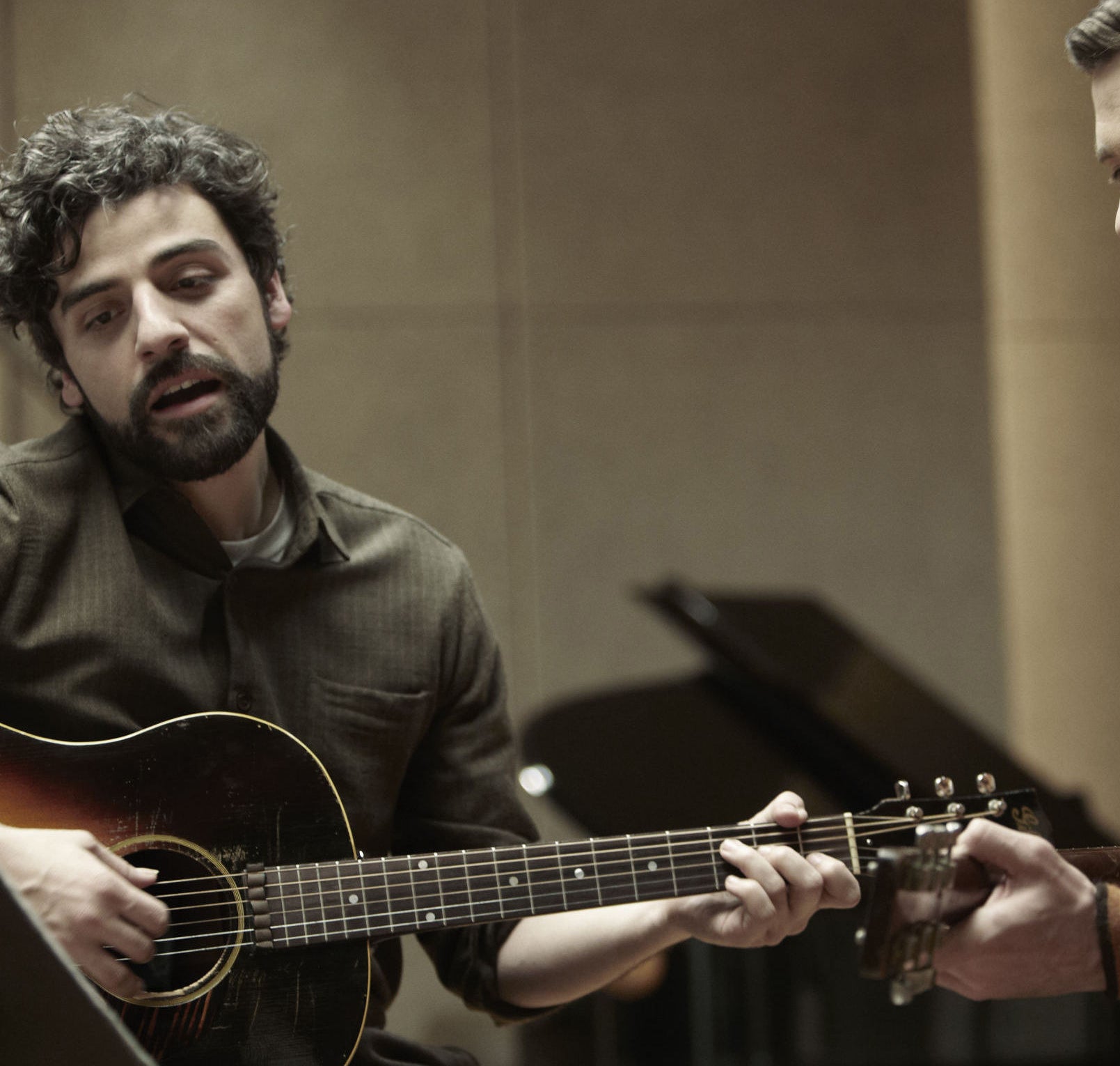 Oscar Isaac holding an old guitar and singing in a 1960s recording studio