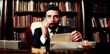 Oscar Isaac sitting at an old desk, licking his fingertips