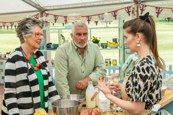 Paul Hollywood glares at a contestant while she explains her bake to a smiling Prue