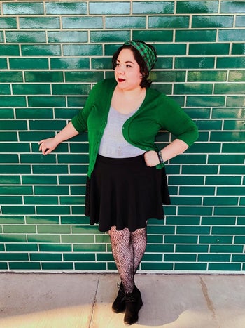 reviewer wears green cardigan and black flared skirt with lacy tights and booties