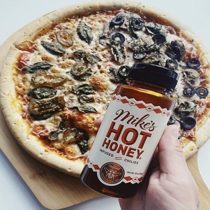 reviewer holding mike's hot honey with a pizza in the background