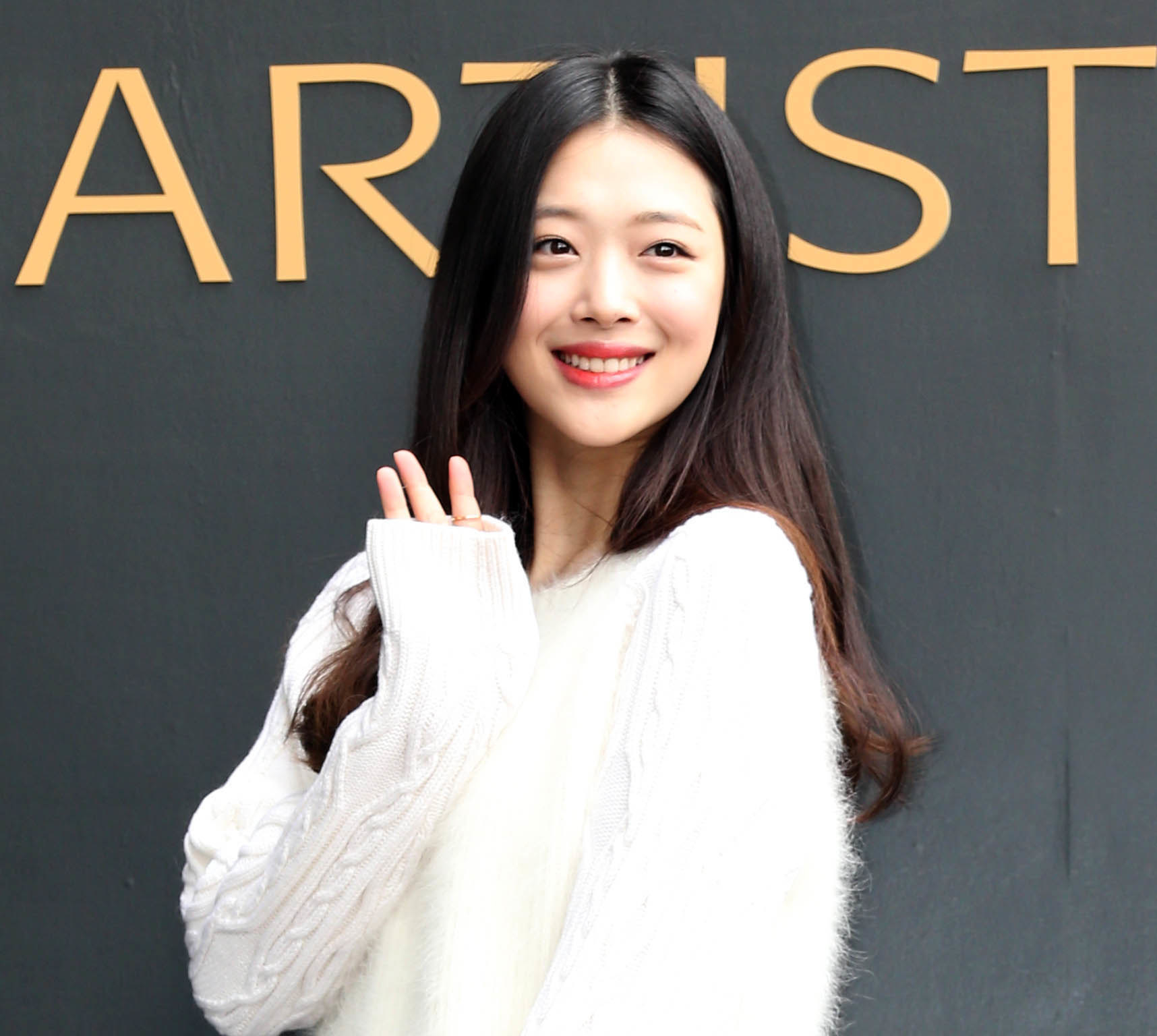 Jinri Choi waves at the camera with her right hand.