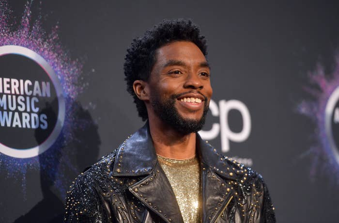 Chadwick Boseman wears a studded leather jacket and poses with a big smile.