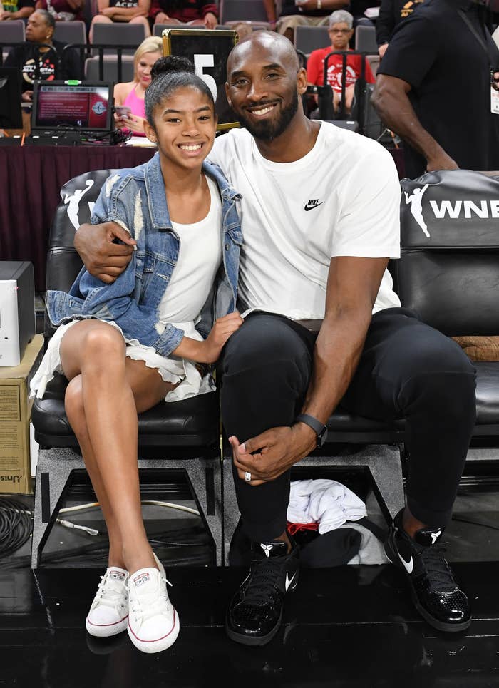 Kobe Bryant wraps his around daughter Gigi in the front row of a basketball game.