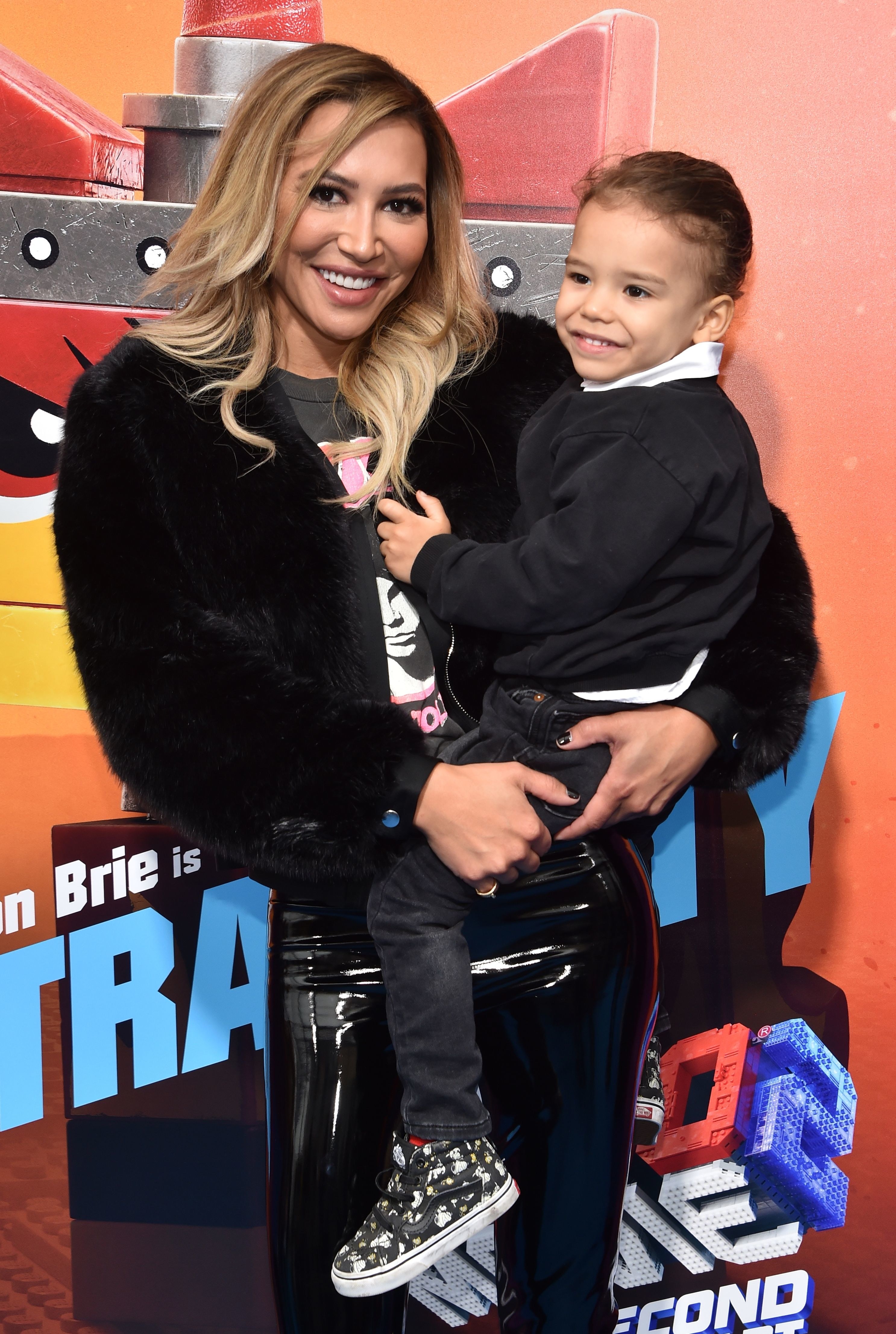 Naya Rivera holds her son Josey up to her, while both smile warmly.