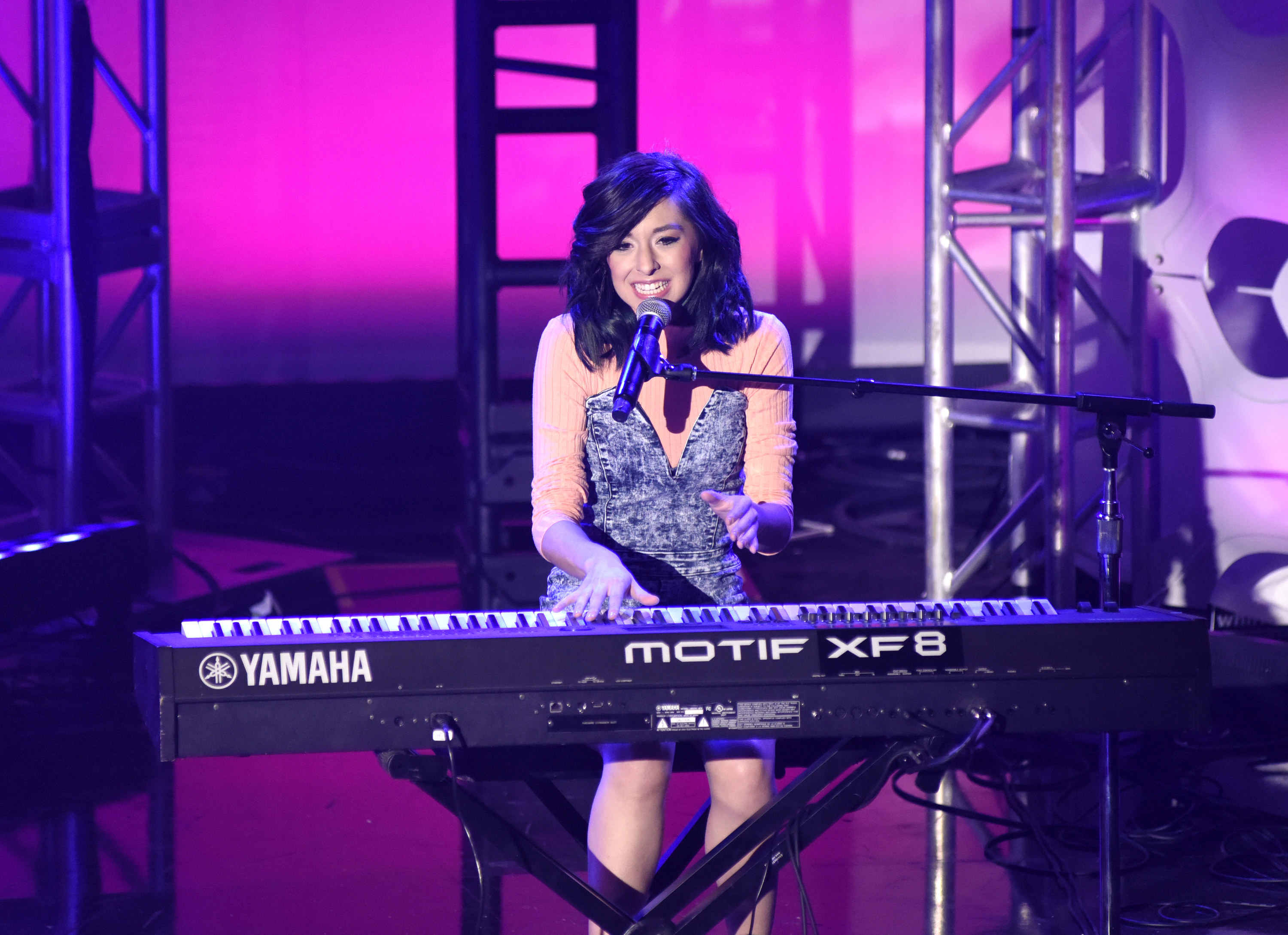Christina Grimmie sits in front of and plays an electronic keyboard while singing at a concernt.