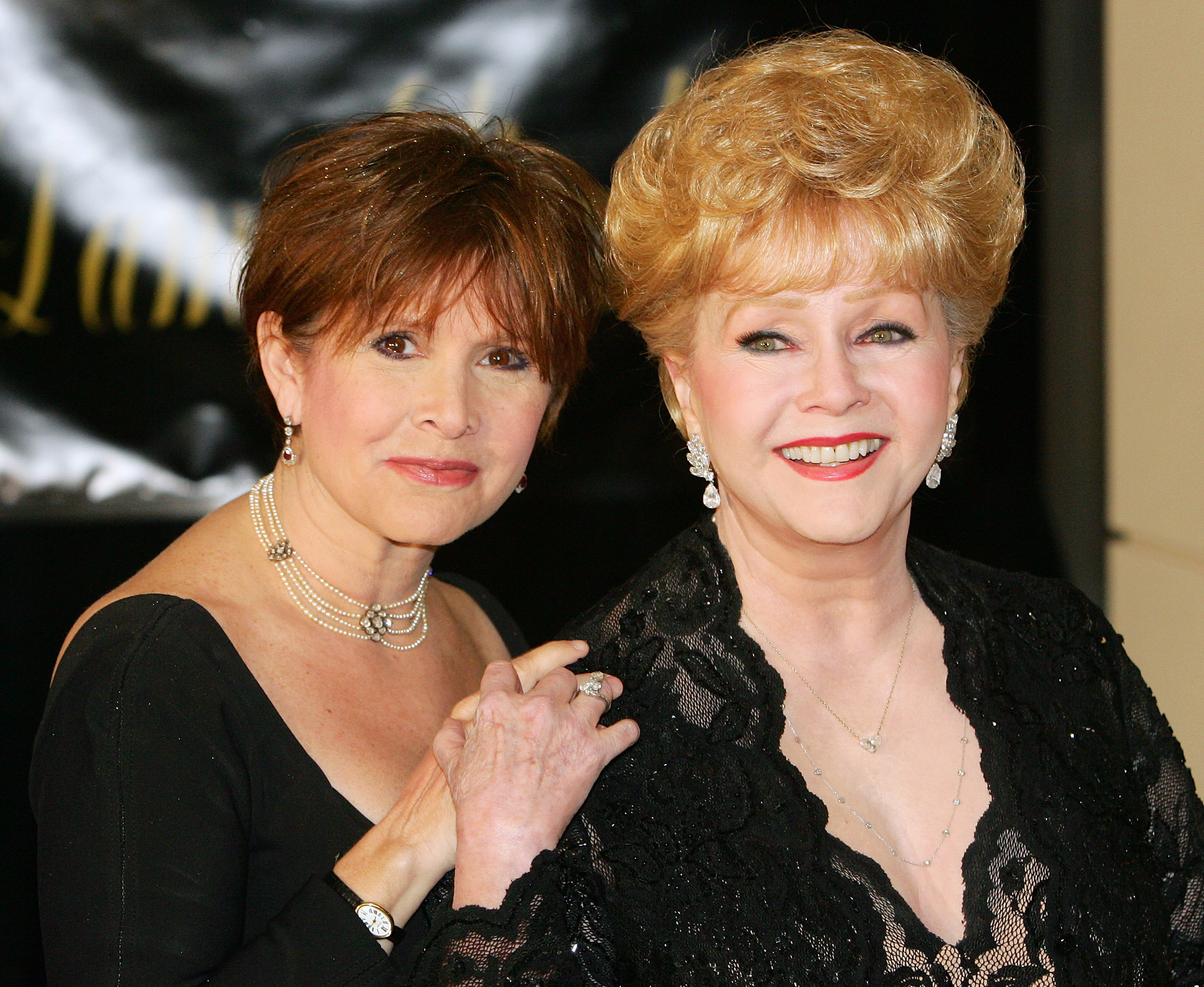 Carrie Fisher stands to the right of her mother, Debbie Reynolds. Both are dressed up for an event.