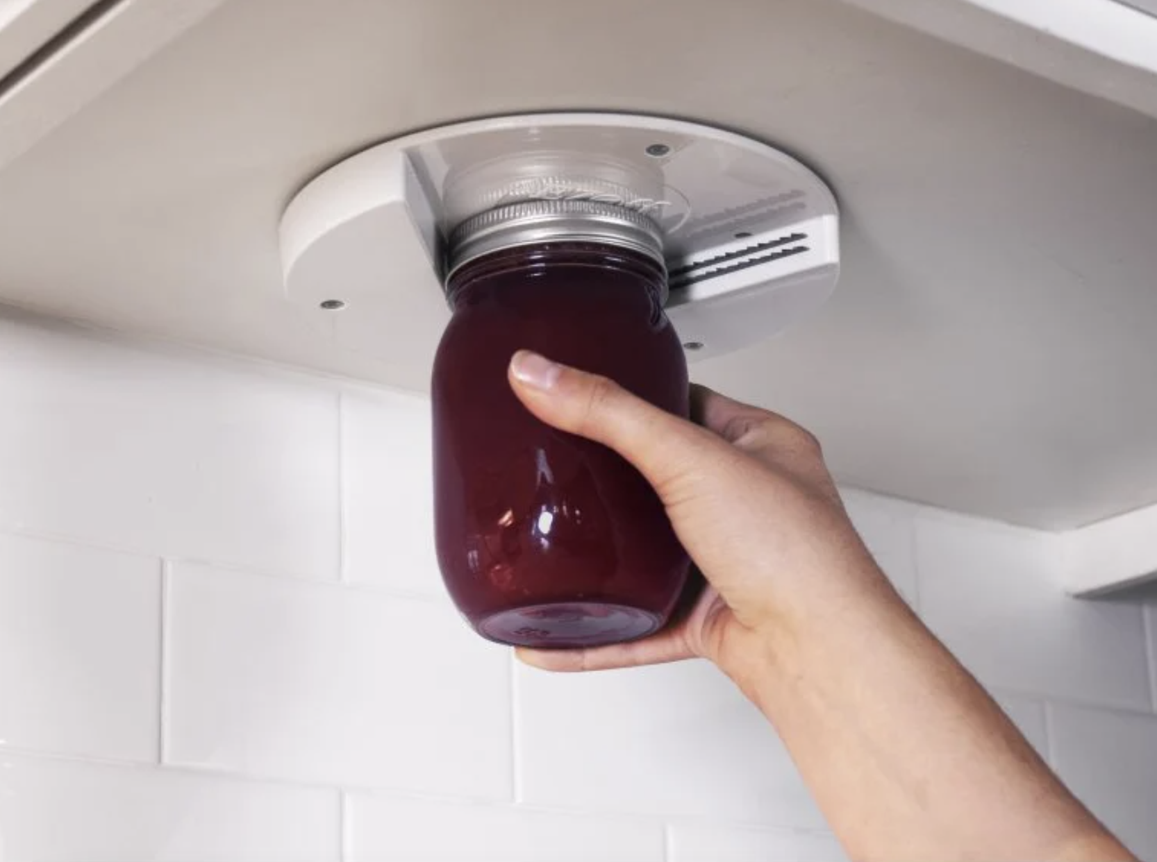 a model&#x27;s hand places a jar into the under-the-counter jar opener