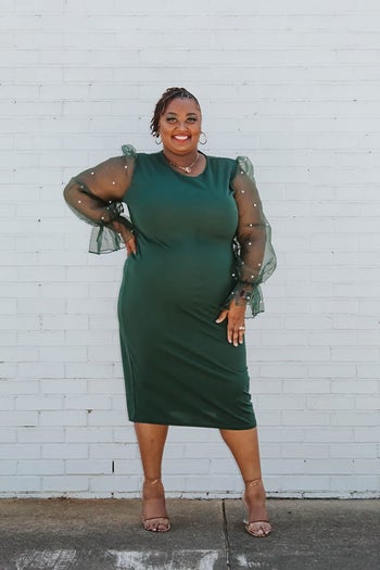 Reviewer is wearing a forest green pencil dress with long mesh sleeves with pearl embellishments on them