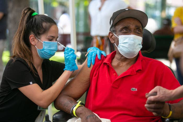 A medical professional with a face mask and rubber gloves injects a syringe into someone's arm