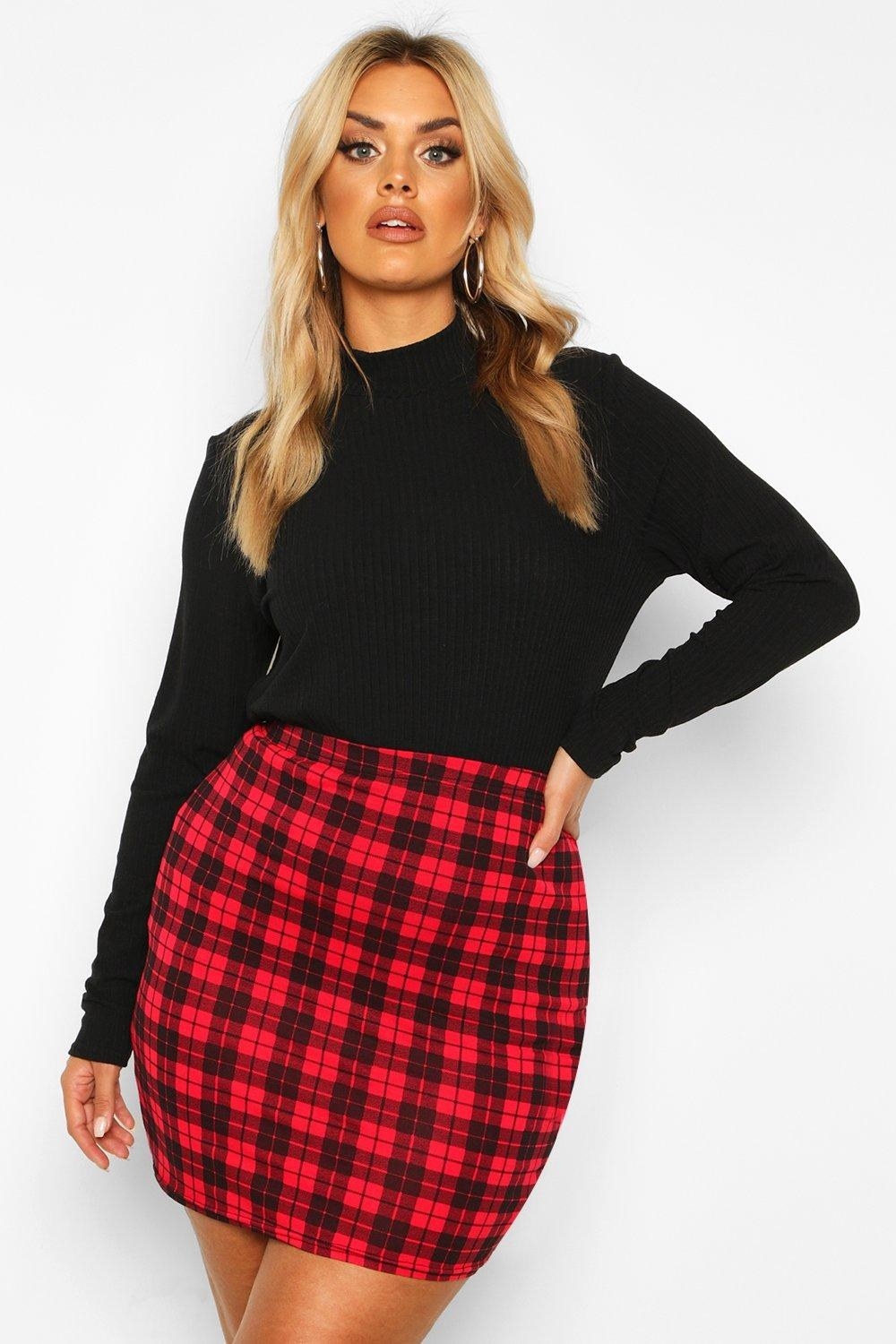 Model is wearing a black long sleeve top and a red and black plaid mini skirt