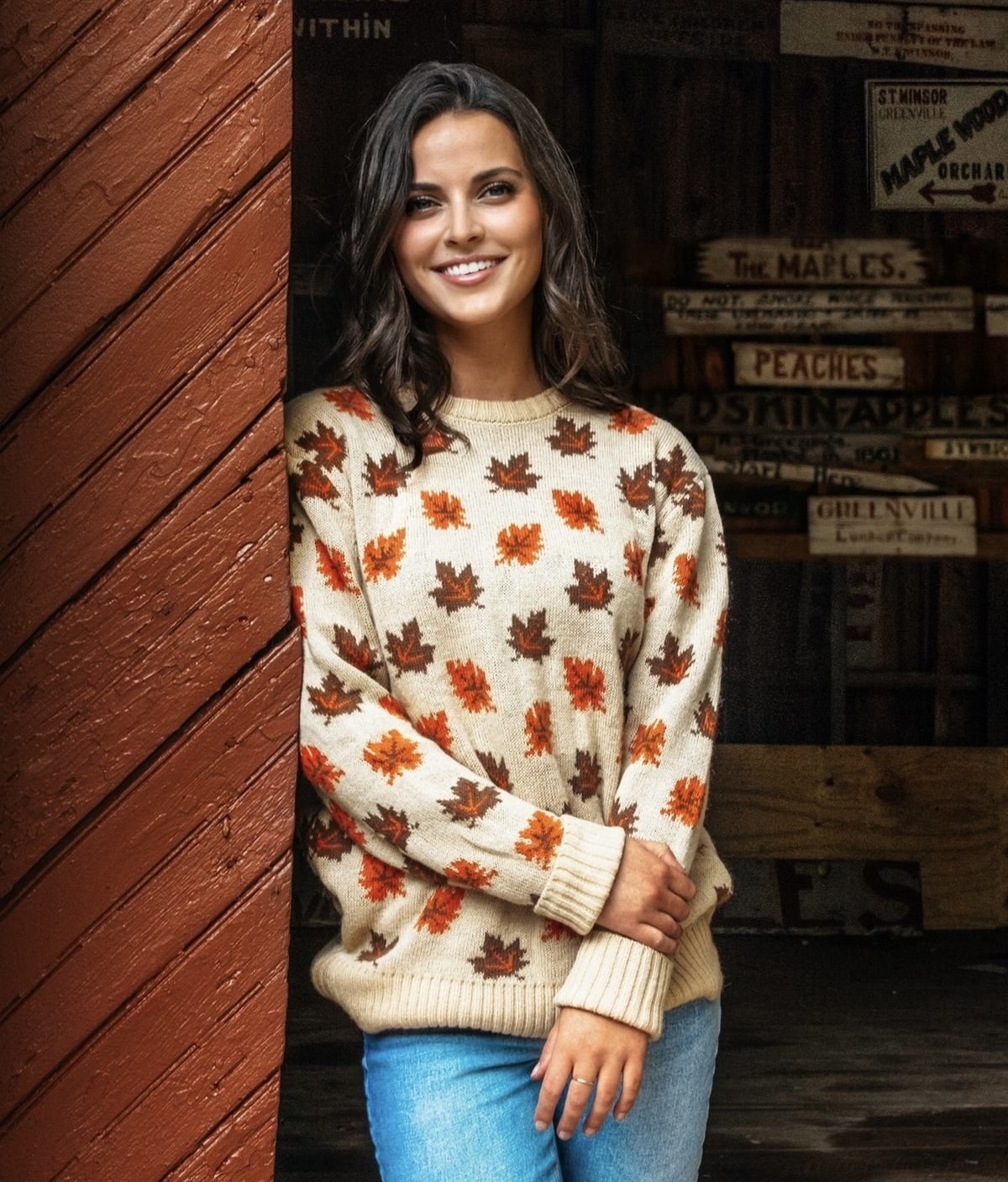 Model is wearing a cream colored sweater with orange and brown leaves printed on it
