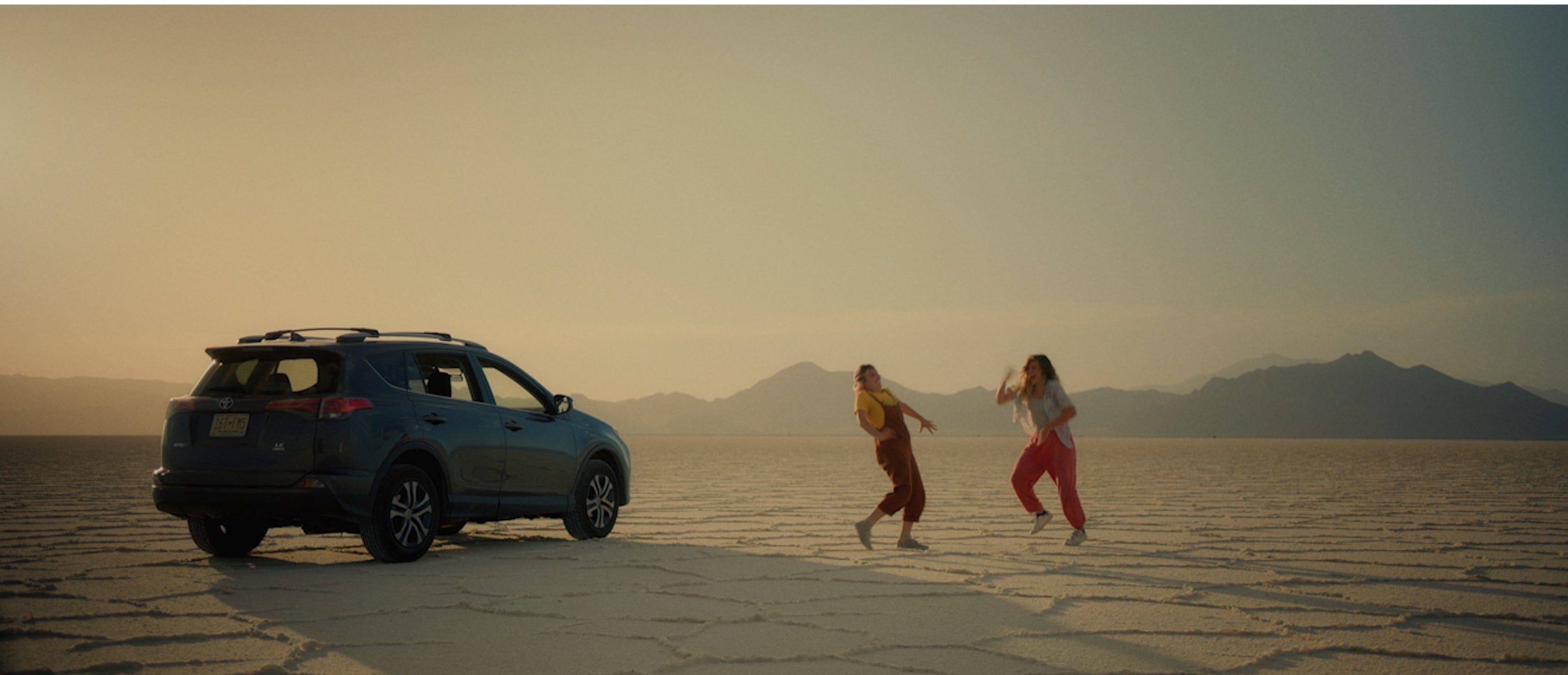 The sisters dancing in the middle of the desert next to a car