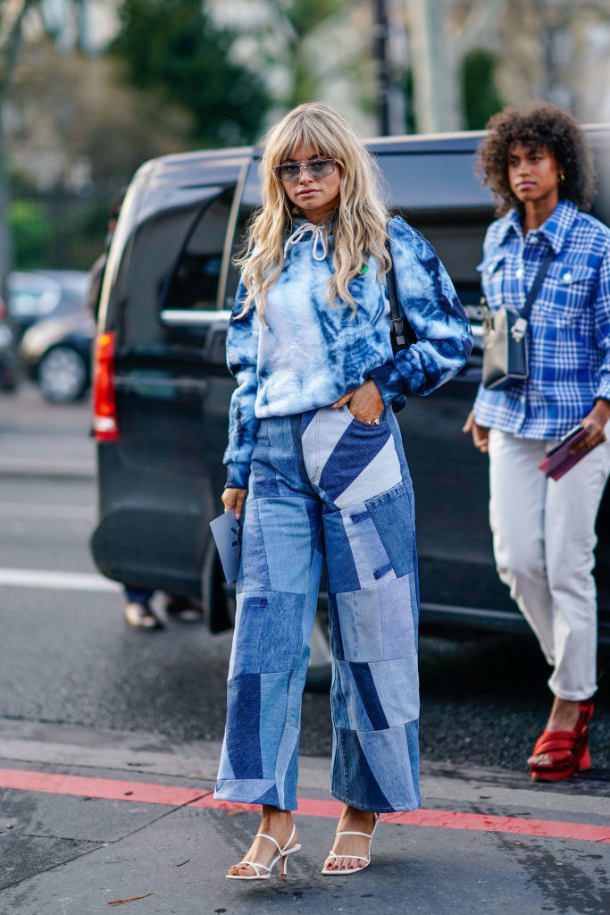 Claire Rose Cliteur wears sunglasses, a blue tie-and-dye top, and blue patchwork flare jeans