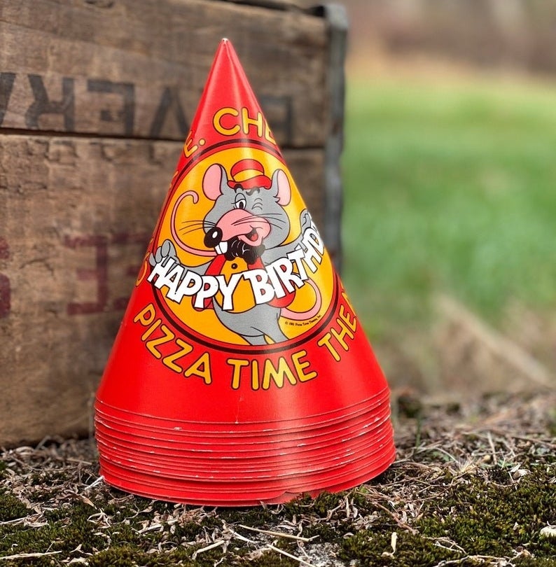 A stack of red birthday party hats with Chuck E. winking on it and holding a happy birthday cutout