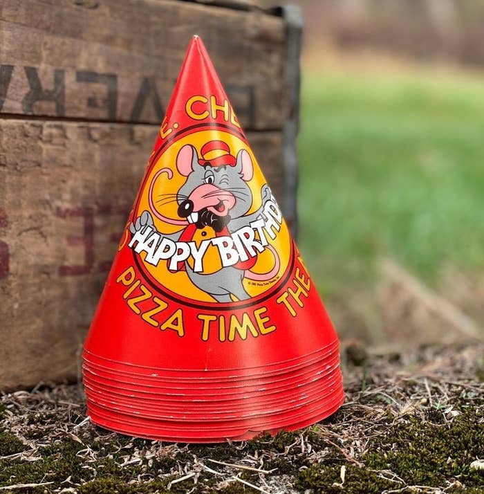A stack of red birthday party hats with Chuck E. winking on it and holding a happy birthday cutout