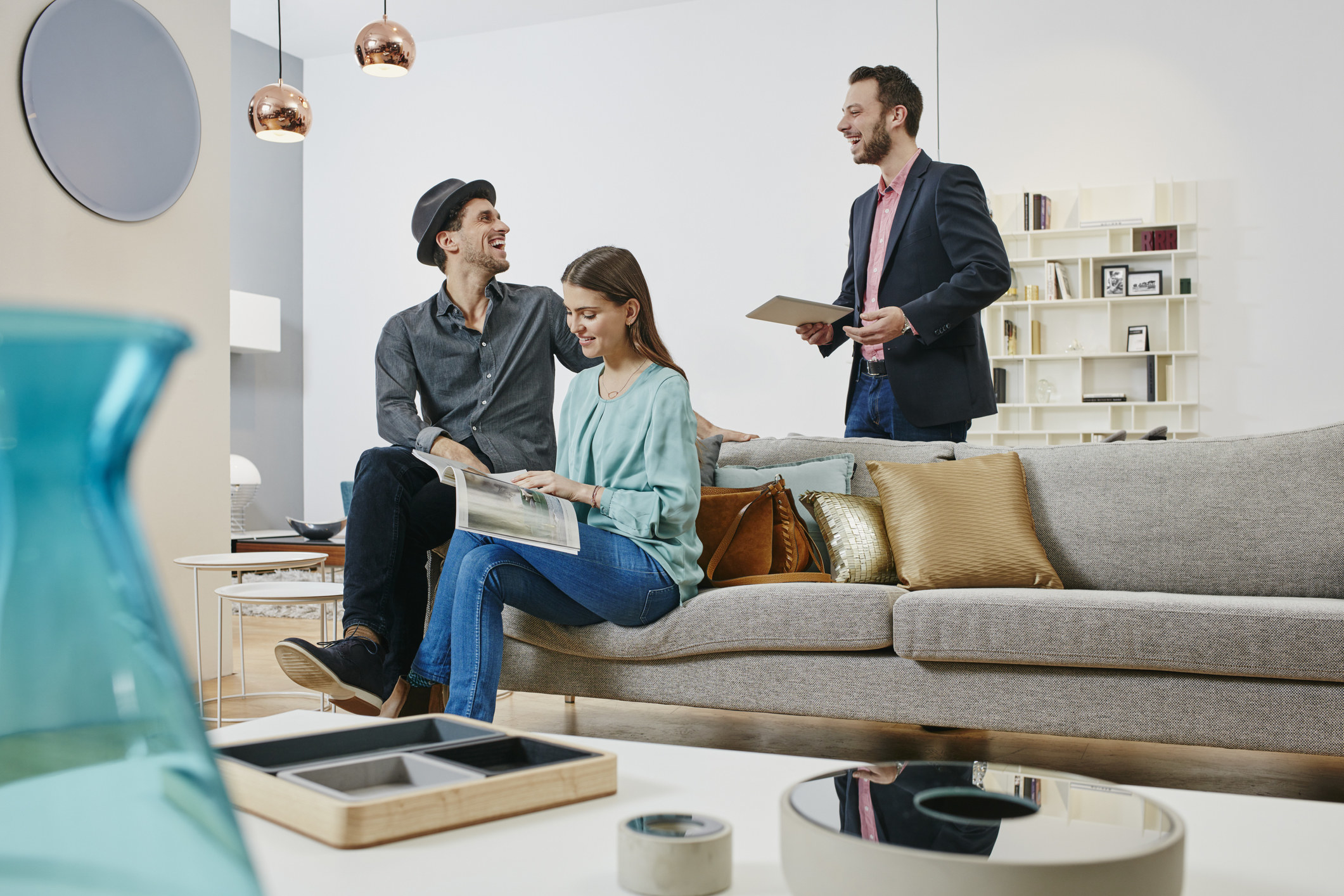 Three people having a conversation as two of them sit on a couch and browse a magazine