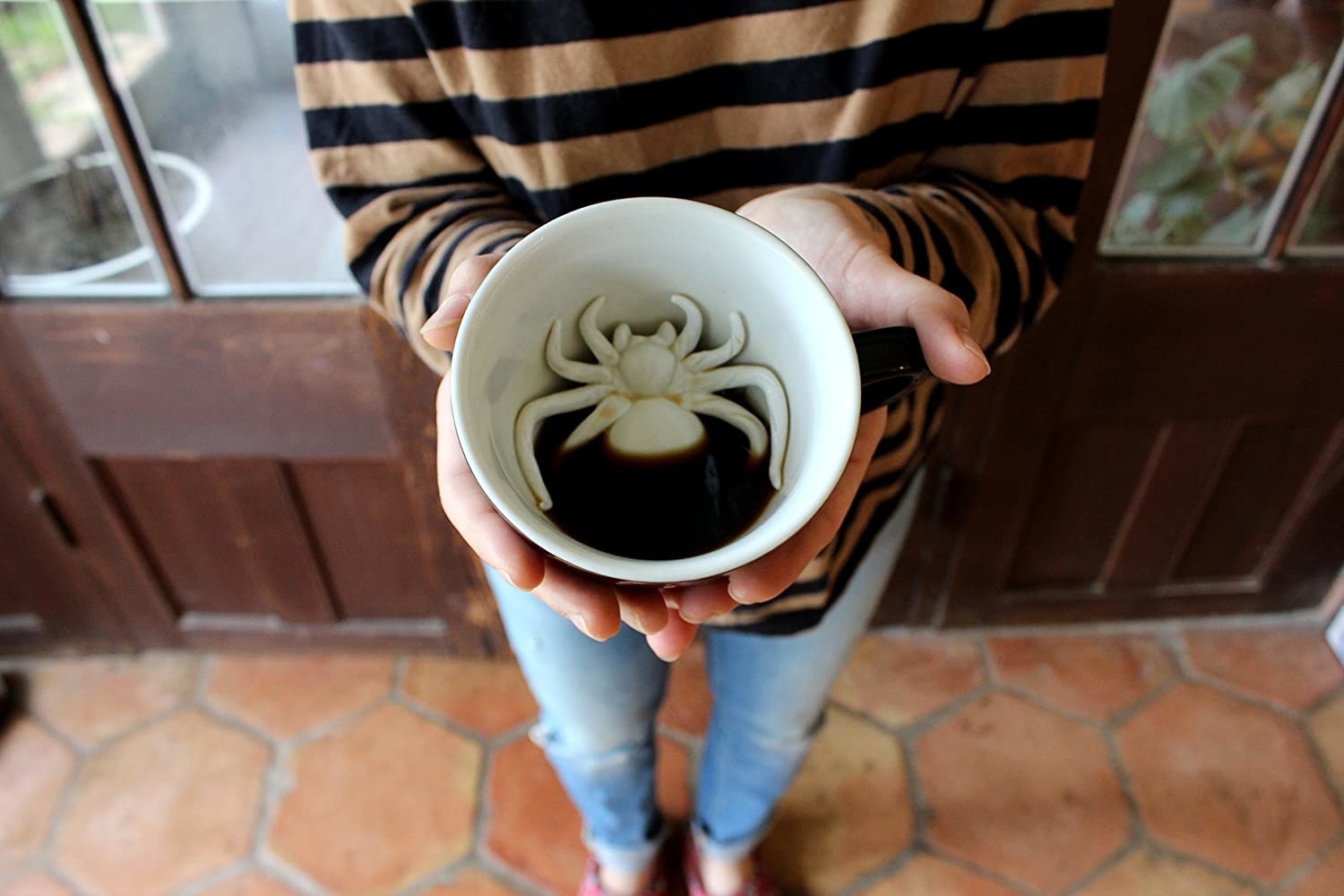 A person holding a mug with a spider revealed under their coffee