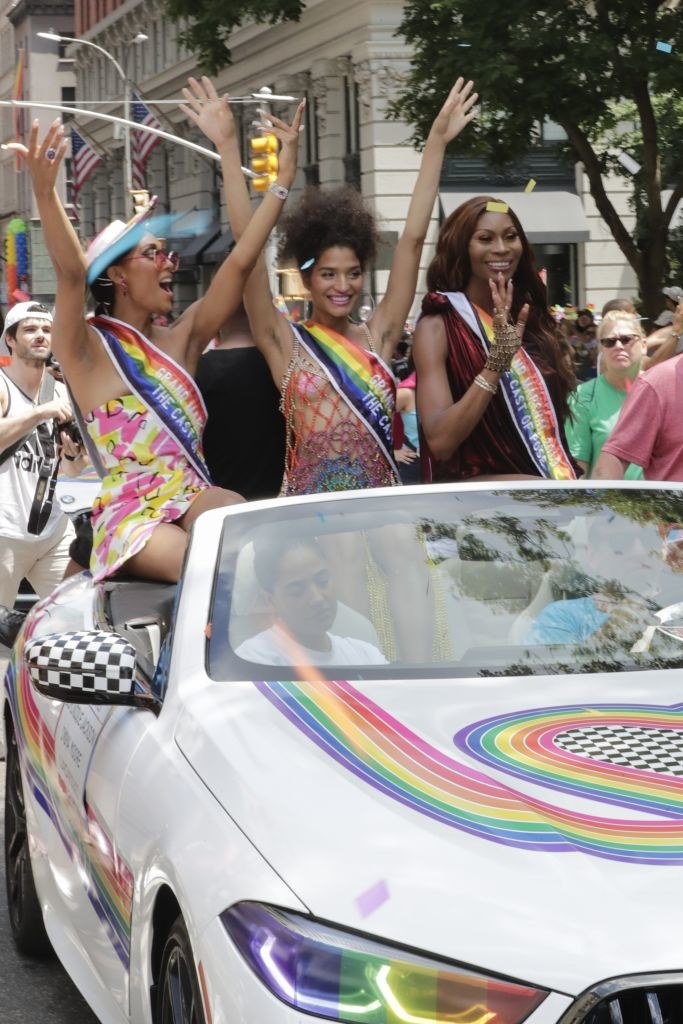 Mj, Dominique Jackson, and Indya Moore wave to the crowd and smile as they sit in a rainbow-decked BMW at Pride