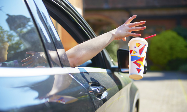 A person throwing a drink cup out the window of the front passenger side