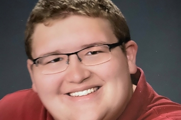 A boy in a red polo shirt smiles at the camera