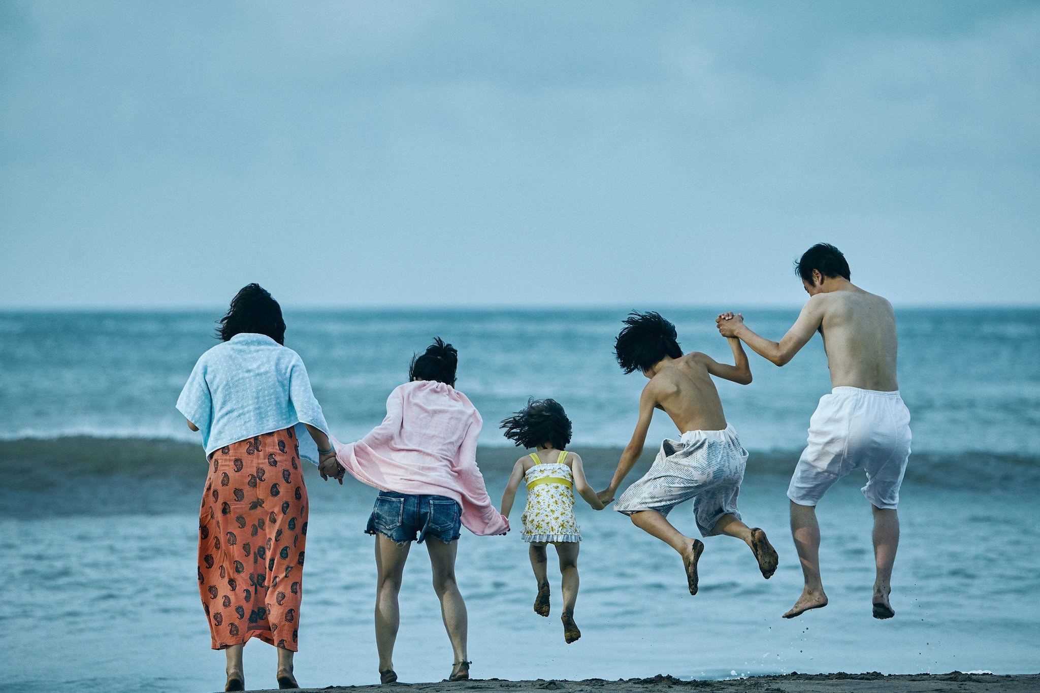a family of five holds hands, jumping into water