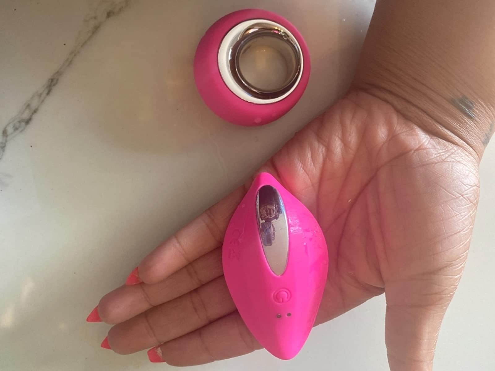 A reviewer holding the curved vibrator with slight points on either end and the matching circular remote