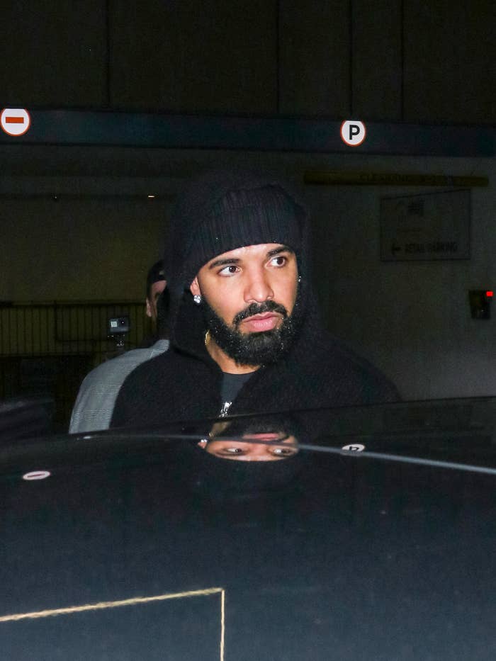 Drake wearing a knit hat and hoodie near a car