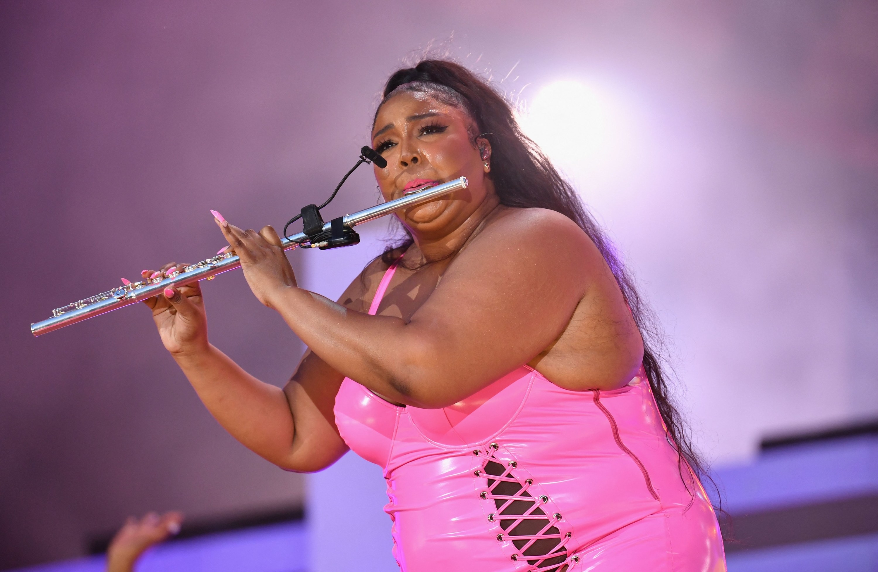 Lizzo plays a flute onstage in a pink bodysuit