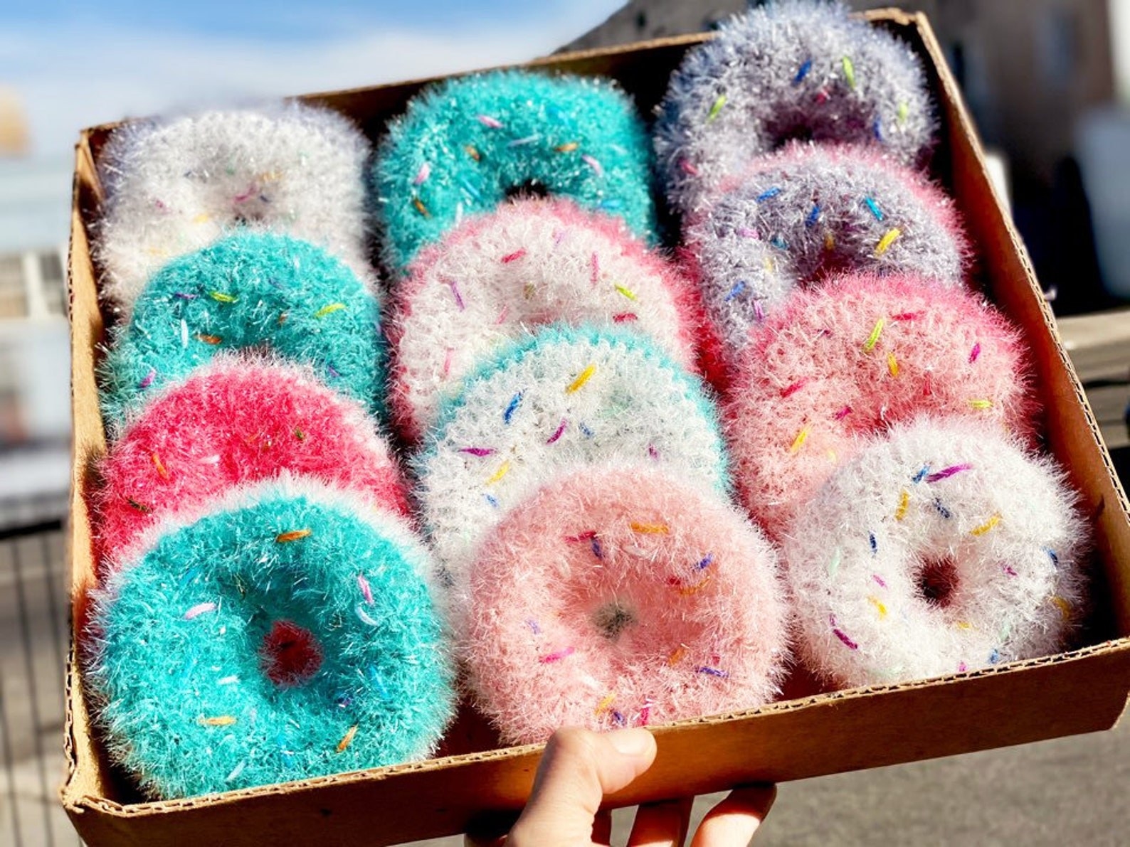A box of scrubbers shaped like donuts with sprinkles in blue, pink, purple, and white color combos
