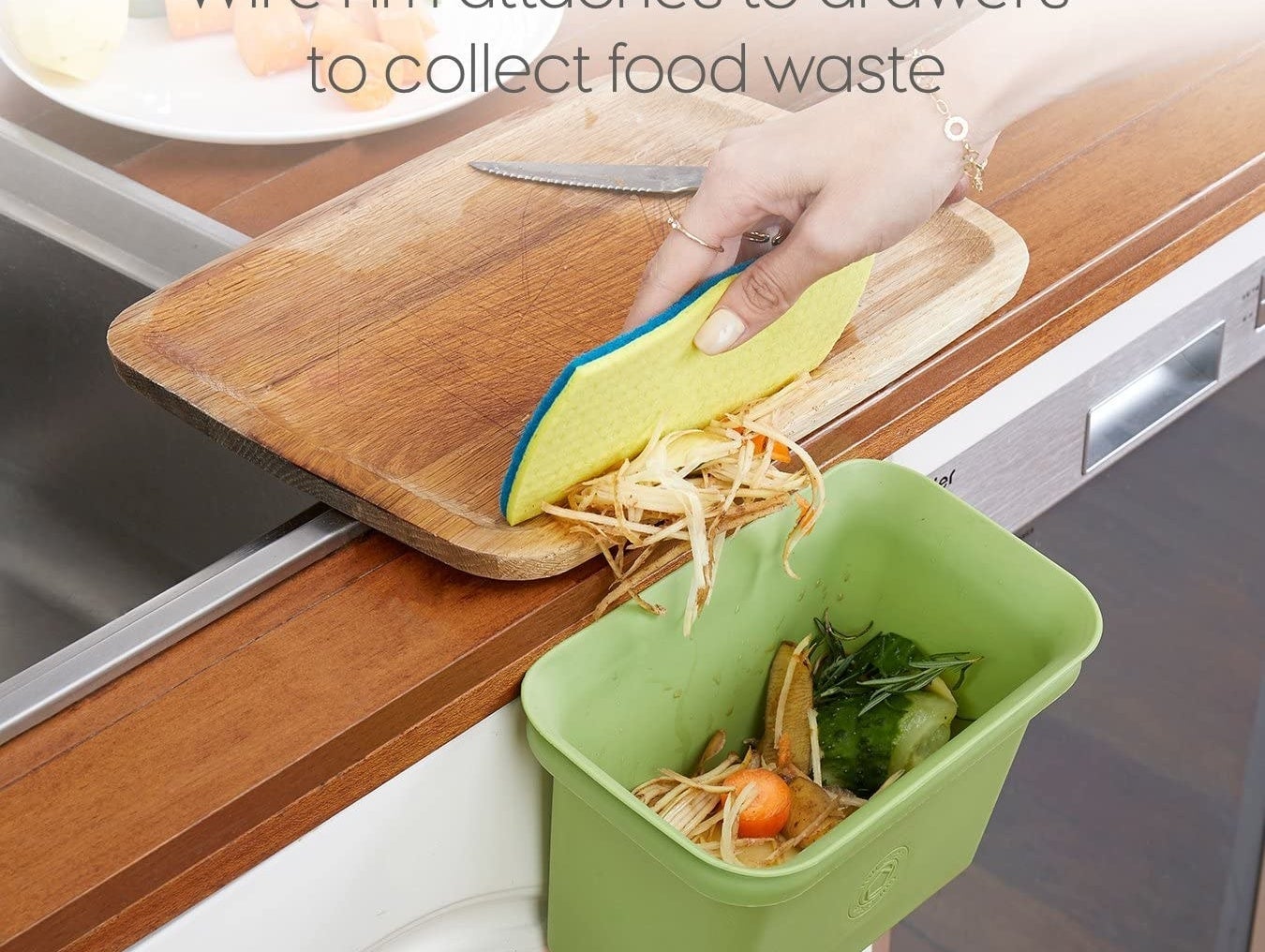 A person scraping vegetable scraps in a bin hanging off the edge of a counter
