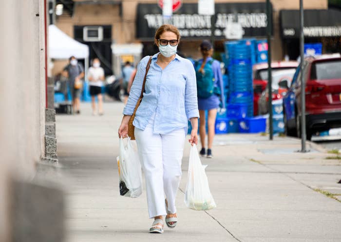 A person wearing a face mask walking down a sidewalk as they carry bags of groceries