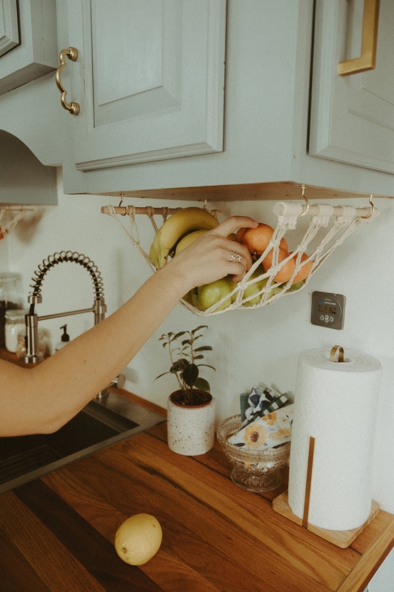 person placing fruit in a hammock hanging down from the bottom of a cabinet