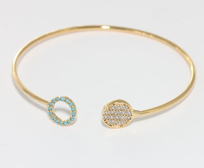 thin gold open bracelet with circular design on each side, one hollow trimmed with teal gems and the other filled in with clear gems