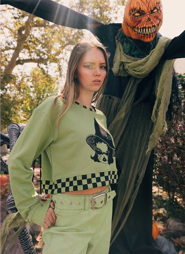 a model wearing the cropped hoodie next to halloween decorations