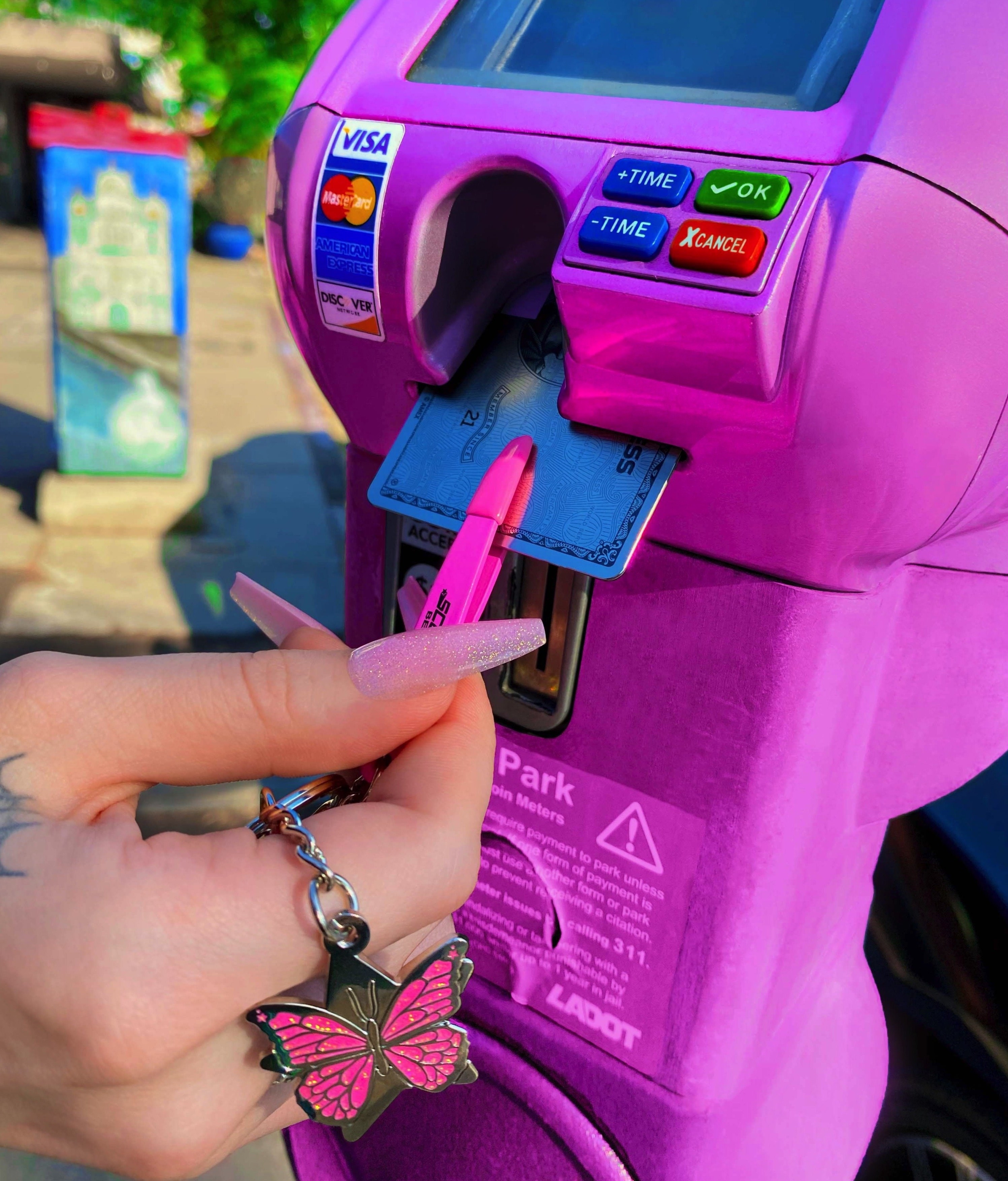 person using a pair of tweezers on a keychain to pull a credit card in and out of a parking meter