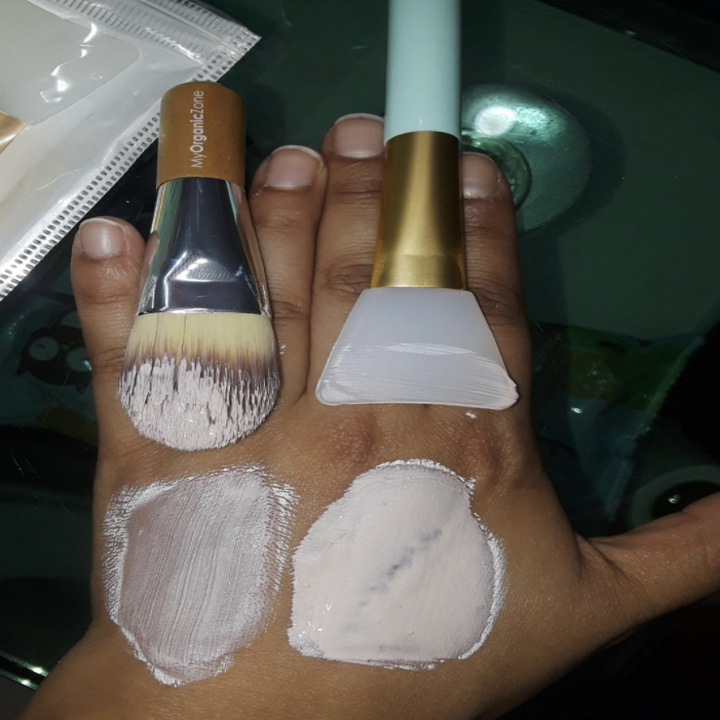 reviewer's hand comparing a strip of foundation with a bristle brush, light coverage. the same strip done with silicone brush full coverage. 