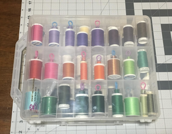 plastic organizer with different compartments with various spools of threads on bobbins stored inside