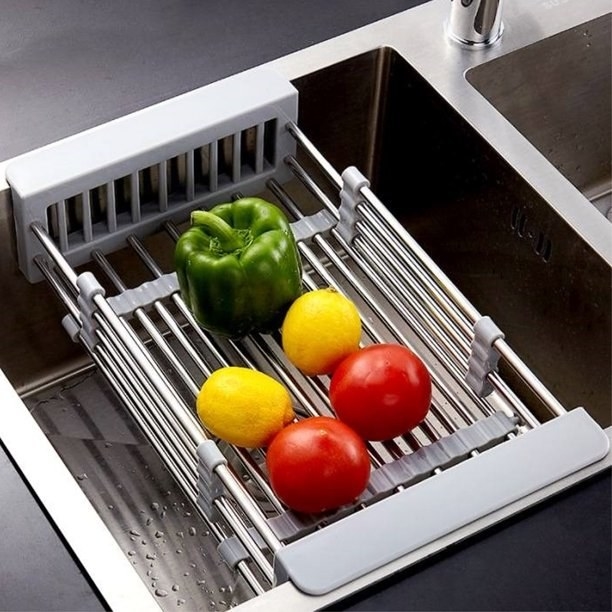 Dish drying rack inside sink with a green pepper, two lemons and tomatoes in it.