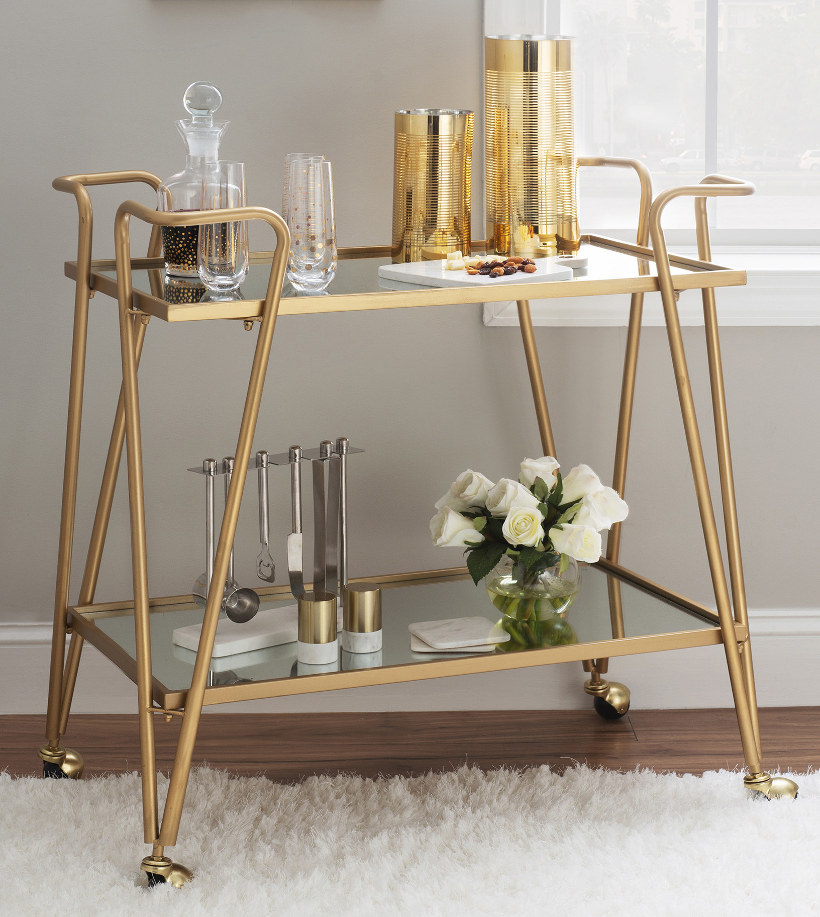 Gold bar cart holding glassware, accessories and flowers.