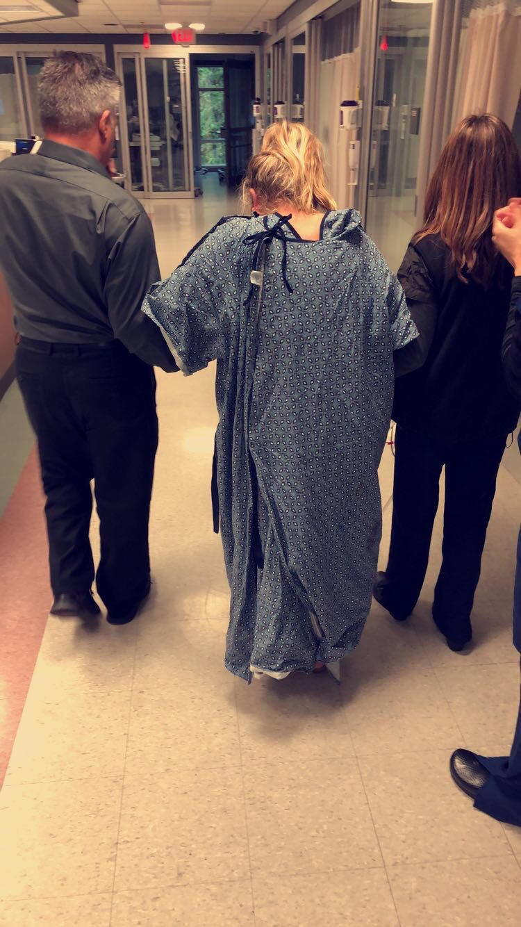 Sam walking through the hospital in a hospital gown with her dad and a nurse
