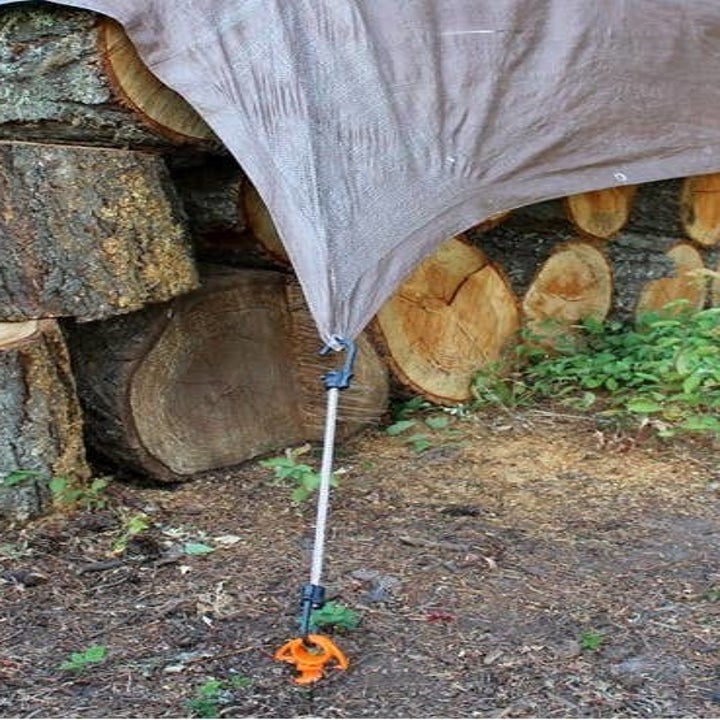 the ground screw anchoring a tarp over a pile of wood