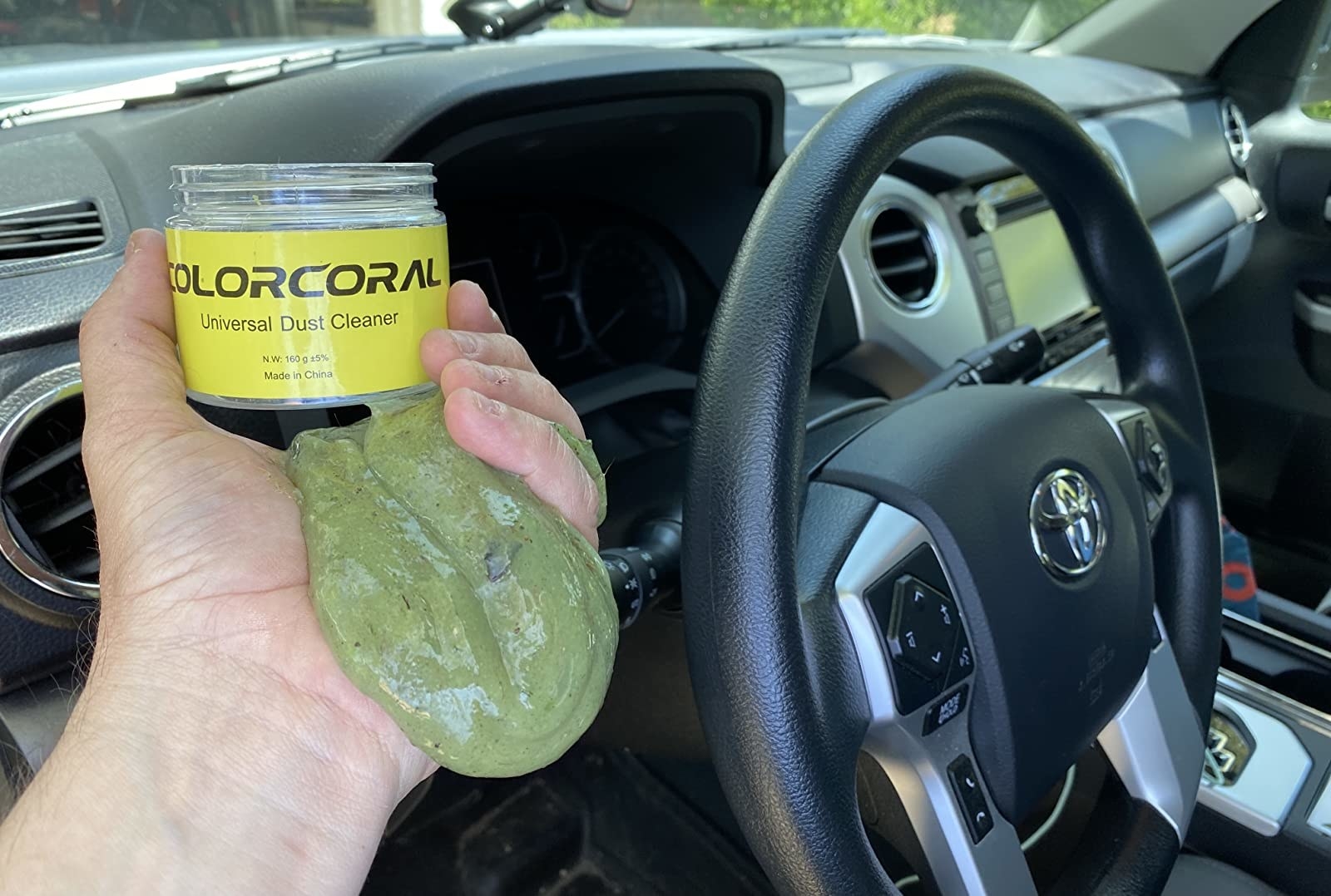 reviewer holding the cleaning goo with dirt and pollen on it after cleaning a steering wheel