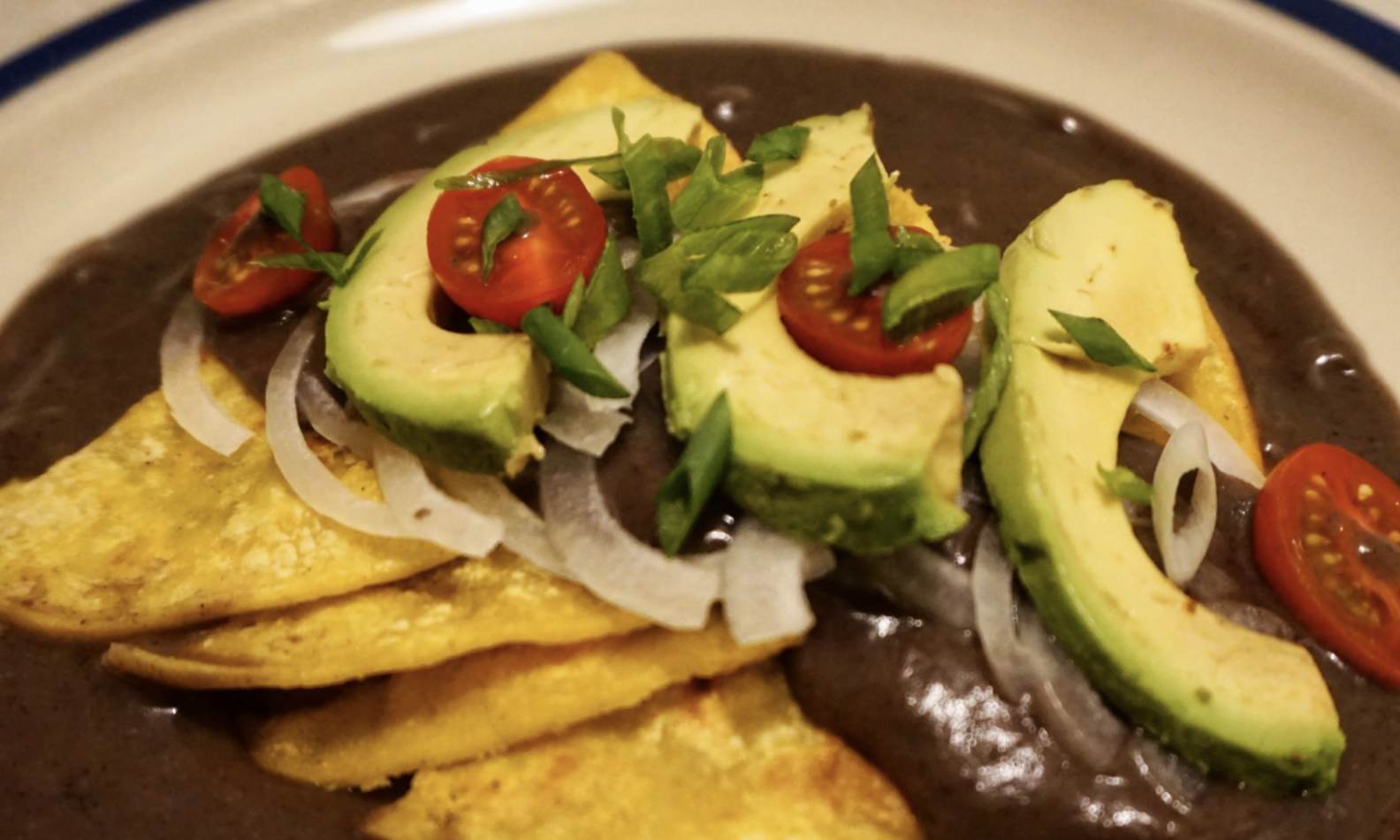 Black bean puree with tortillas, tomatoes, and avocados on top of it