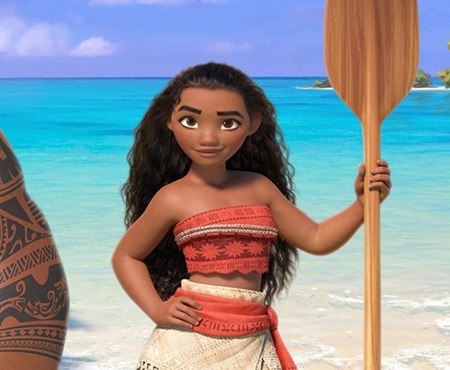 moana stands in front of the ocean, hand on hip, other hand holding canoe paddle