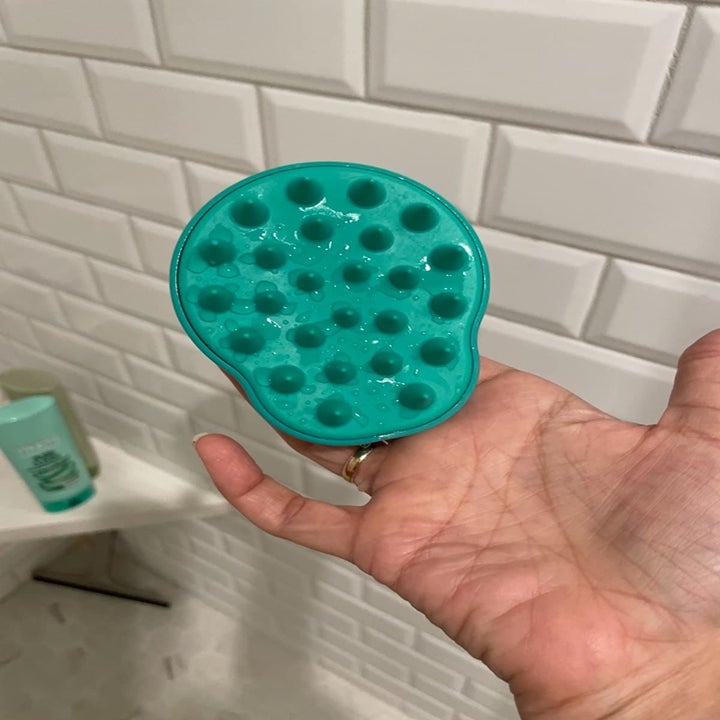 reviewer holding the teal shampoo brush and scalp massager