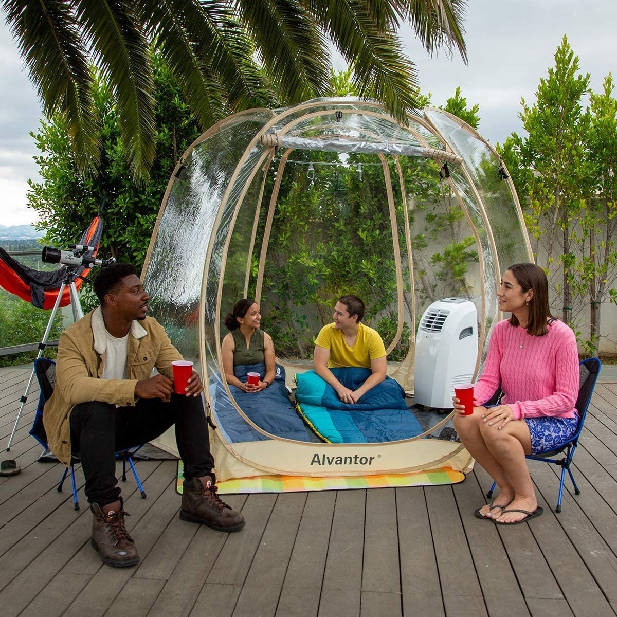 models sit inside clear weather pod with sleeping bags and portable heater